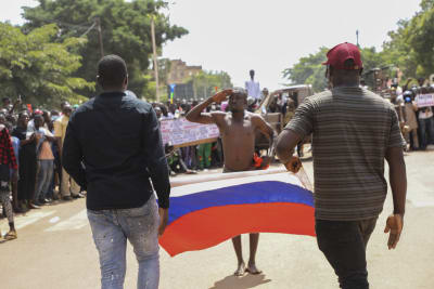 Två män bär en rysk flagga mellan sig i Ouagadougou i Burkina Faso. En tredje gör honnör.