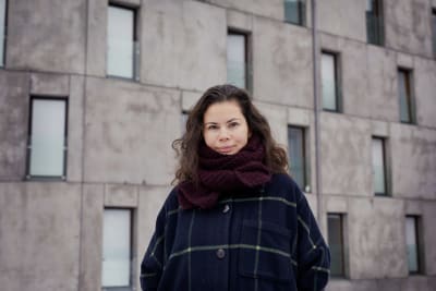 Liza Alexandrova-Zorina står framför en betongfasad. Hon har en rutrandig jacka och en halsduk på sig.