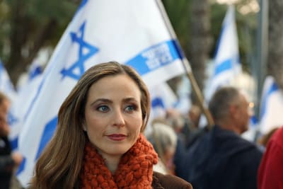 En kvinna tittar mot höger med israeliska flaggor i bakgrunden.