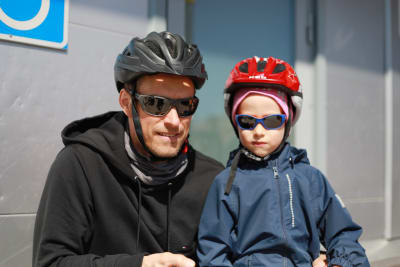 En man och en liten pojke, båda med solglasögon och cykelhjälm, tittar in i kameran