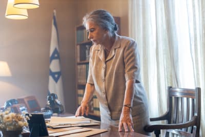 Helen Mirren som Golda Meir står lutad över ett skrivbord med den israeliska flaggan i bakgrunden.