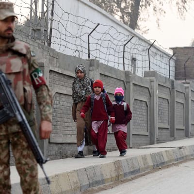 Pakistanilaisia sotilaita seisoo kaduilla vartiossa, kun lapset kävelevät kouluun Peshawarissa. 