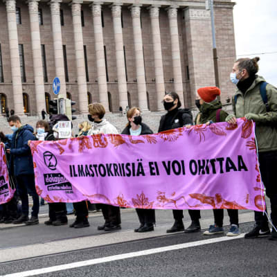 Demonstranter som står på Mannerheimvägen och håller upp en banderoll.