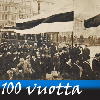 Mustavalkoinen valokuva väkijoukosta, joka marssii kadulla ison Viron lipun jäljessä.