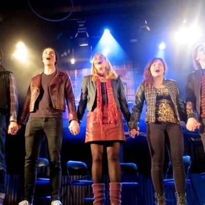 Kuusi näyttelijää käsi kädessä laulavat näyttämän kirkkaissa valoissa