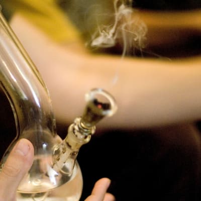 Lasinen kannabispiippu, jota pitelee naisen käsi.