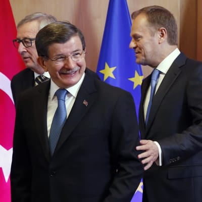 Juncker, Davutoğlu ja Tusk poseeraavat Turkin ja EU:n lippujen edessä.