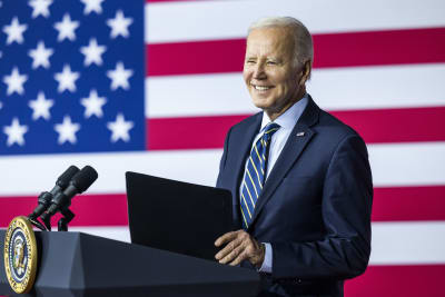 Joe Biden ler medan han står vid ett talarpodium. I bakgrunden USA:s flagga.