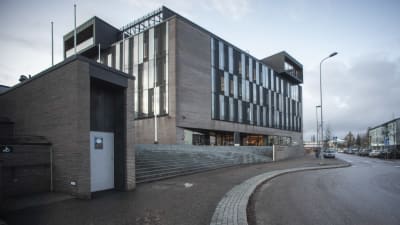 En futuristisk grå byggnad. I förgrunden en bilväg. 