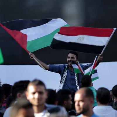 Mies heiluttaa palestiinalaisten ja Egyptin lippua väkijoukon yläpuolella.