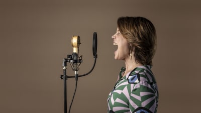 Emma Salokoski sjunger för full hals in i en mikrofon, fotad i profil.