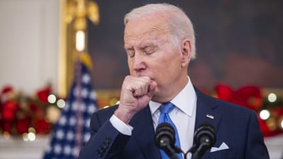 Joe Biden tittar åt sidan medan han hostar i ärmen.