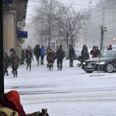 Nainen kerjäämässä kadulla lumisateessa.