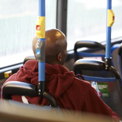 Tummaihoinen mies istuu bussin penkillä.