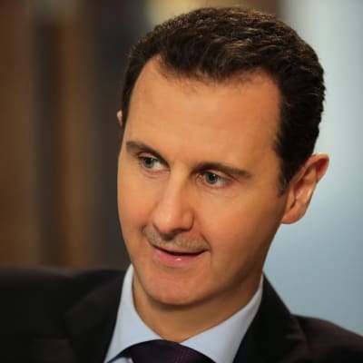 Syyrian presidentti Bashar al-Assad hymyilee. Hänellä on tumma puku.