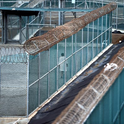 Valkopukuinen vanki kävelee Guantánamon vankileirin pihamaalla.