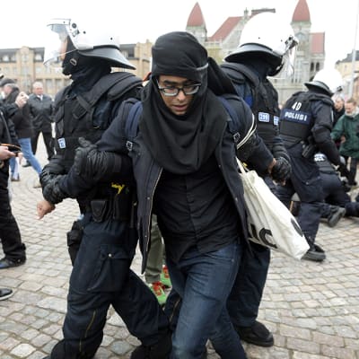Poliisit ottavat kiinni mielenosoittajaa vappumarssilla.