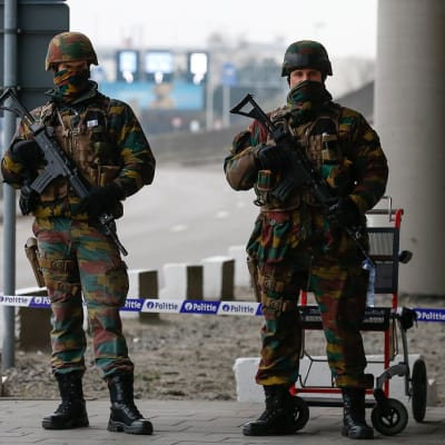 Kaksi raskaasti aseistettua univormupukuista, naamioitua sotilasta lentokentän edessä. 