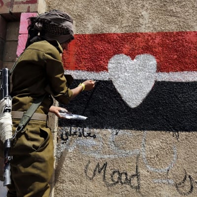 Naamioitunut ja aseistautunut sotilas maalaa muuriin Jemenin lippua, jonka keskellä on sydän.