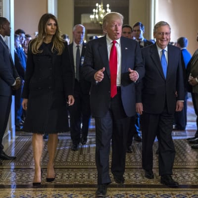 Trump kävelee käytävällä vaimonsa Melanian ja McConnellin kanssa näyttäen peukkua. Seinänvierillä sivustakatsojia.