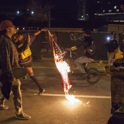 Yöllinen kuva, jossa juokseva mielenosoittaja roikottaa perässään palavaa lippua.