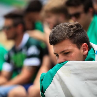 Sureva poika istuu stadionilla ja on kietoutunut valkovihreään jalkapallojoukkueen lippuu.n