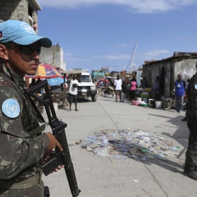 sSniset YK-lippikset miehillä päässä, aseet kädessä, kadulla Haitissa