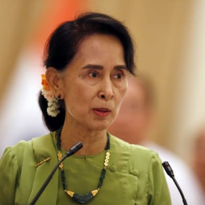 Aung San Suu Kyi vaaleanvihreässä asussa puhuu edessään oleviin mikrofoneihin.