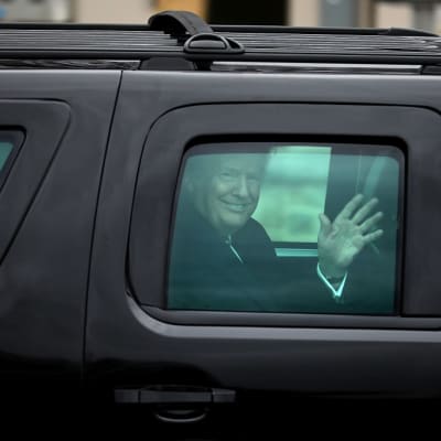 Trump vilkuttaa massiivisen mustan auton ikkunasta hymyillen leveästi.