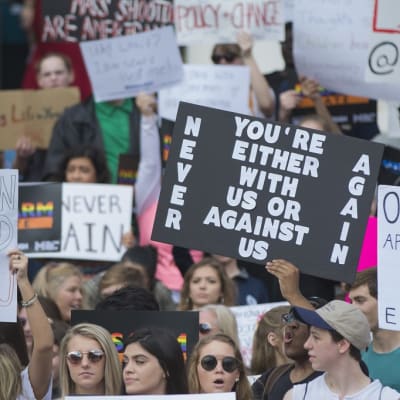 Joukko nuoria pitelee kylttejä mielenilmauksessa. Kuvan keskellä olevassa kyltissä lukee: "Olet joko meidän puolellamme tai meitä vastaan."