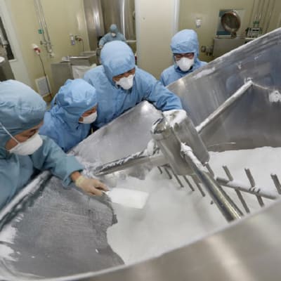 Työntekijöitä valmistamassa klorokiinia kiinalaisessa lääketehtaassa. Kuvassa neljä suojapukuihin pukeutunutta ihmistä. Sammiossa on valkoista jauhetta, jota he tarkastelevat. 
