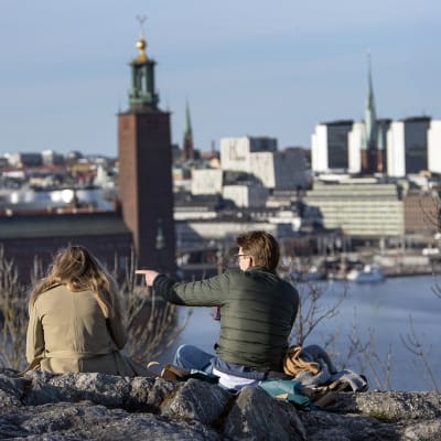 Vierekkäin, selin kameraan, istuvat kaksi ihmistä katselevat Södermalmin kallioilta Tukholman keskustaan päin.