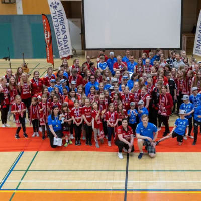 Iso joukko Woman Volleyn ja Napapiirin kettujen pelaajia katsoo kameraan alhaalta ylös liikuntasalin lattialta.
