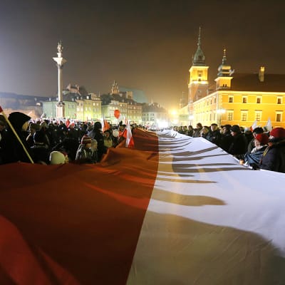 Muistomarssille osallistuneet ihmiset pitelevät suurta Puolan lippua.