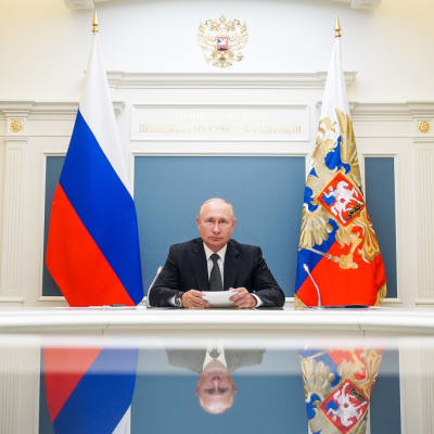 Putin pöydän ääressä. Hänen kuvansa heijastuu pöydän kiiltävältä pinnalta.