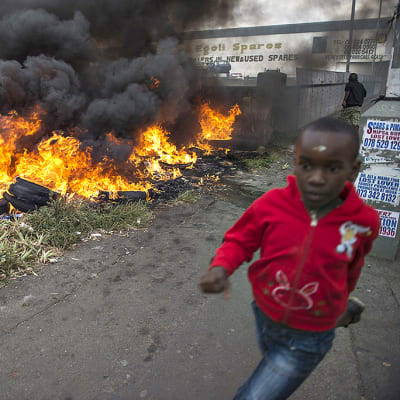 Lapsi juoksee palavien autonrenkaiden ohitse Johannesburgin keskustassa.