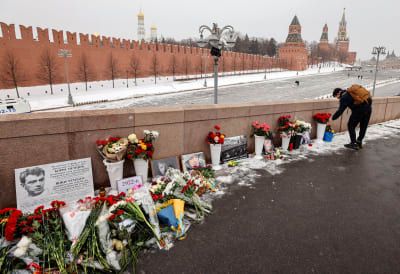 Sillan kivistä kaidetta vasten on aseteltu kukkia ja kuvia Boris Nemtsovista. Mies on kumartuneen kukkien ylle kuvan oikeassa reunassa. Taustalla näkyy Kremlin punainen muuri.