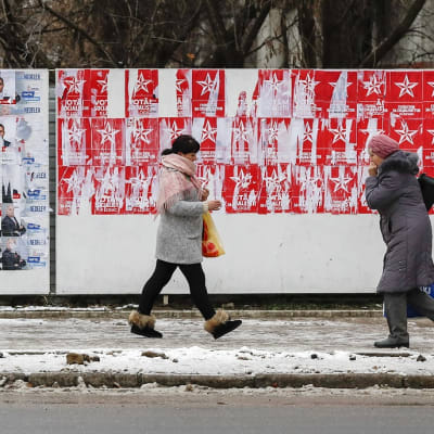 Kaksi naista kävelee vaalijulisteiden ohi talvisella kadulla.