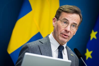 Ulf Kristersson med en svensk flagga och en EU-flagga bakom sig.