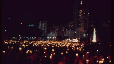 Tusentals människor står på en öppenplats och håller upp ljus. Det är kväll och mörkt.