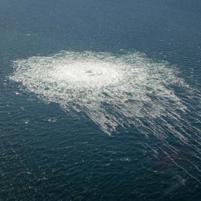 Ett flygfoto av ett runt område i havet som är alldeles vitt av bubblor från en undervattensläcka. Runt den vita rundeln bildas dessutom som en krans av bubblor.
