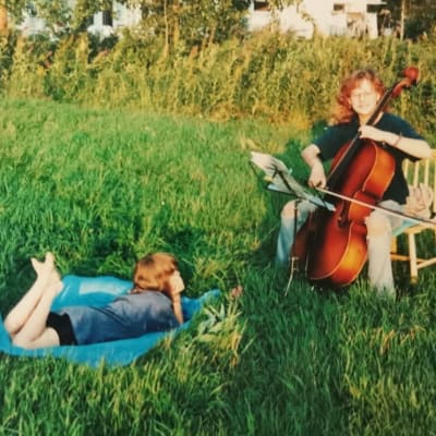 Meer Koutaniemi makaa lapsena kotipellon heinikossa kunnelleen Riikka-siskoa, joka soittaa selloa tuolilla istuen pellon laidassa.