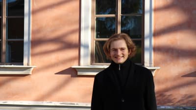Puolalaispianisti Piotr Pawlak kuvattuna Hakasalmen huvilan edustalla. Hän hymyilee ja katsoo hieman kuvaajan ohi.
