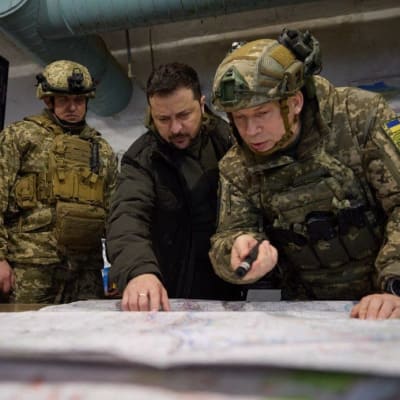 Ukrainas president Volodymyr Zelenskyj studerar en karta tillsammans med militärer i kamouflageuniform.