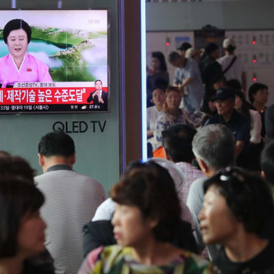 Eteläkorealaiset katsovat televisiota, jossa näkyy pohjoiskorealainen uutisankkuri vaaleanpunaisessa asussa.