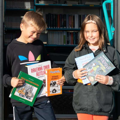 Eino Pärssinen ja Salli Ranta-Eskola pitelevät käsissään kirjoja kirjastoauton ovella.