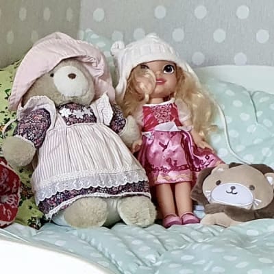 En bäddad säng med en docka, en nalle och ett mjukt lejon placerade på mitten på ett harmoniskt sätt.