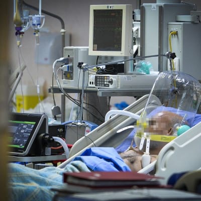 Potilas makaa sairaalavuoteessa hengitysmkoneessa, sängyn ympärillä useita sairaalalaitteita. Kasvot pixelöity. Koronapotilas hengityskoneessa milanolaisessa sairaalassa maaliskuun lopussa.