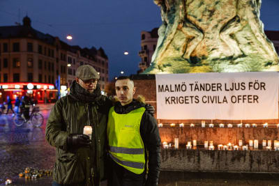 Aron Boklund Tendler och Bassem Nasr står framför ljus och ett plakat där det står Malmö tänder ljus för krigets civila offer.