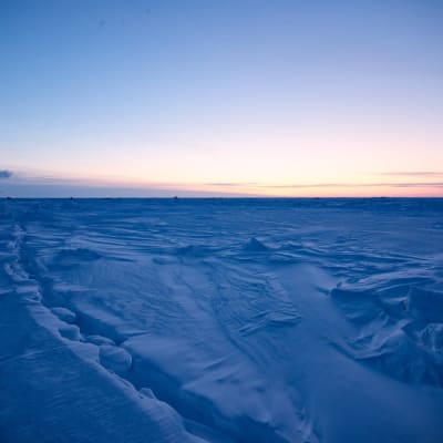 Iso jäälautta ja laiva, taustalla Aurinko hieman horisontin yläpuolella. 